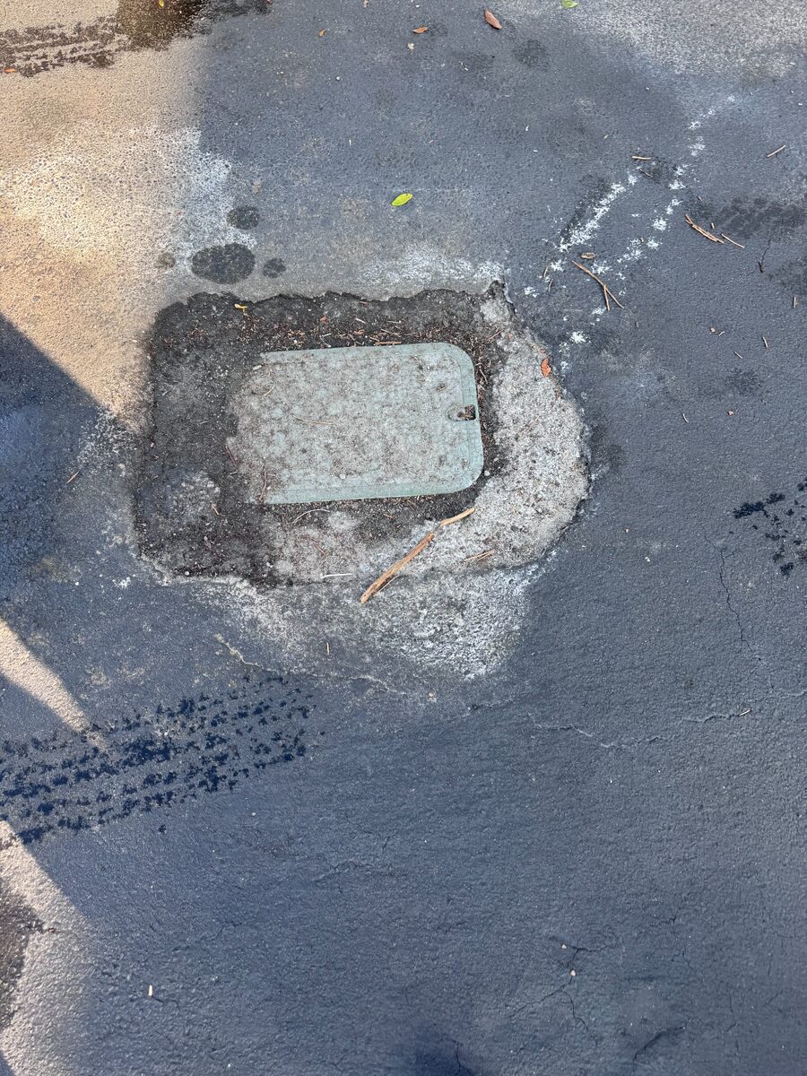 Broken asphalt around a utility access box in a parking lot